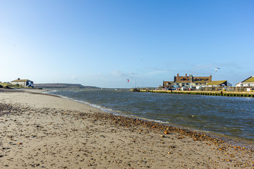 A view of a water channel between Christchurch (UK) harbor and bay with sandy beach and fishering buildings along the banks under a majestic blue sky