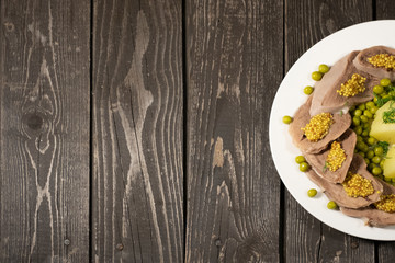 boiled beef tongue with potatoes, green peas, herbs and mustard on dark wooden background 