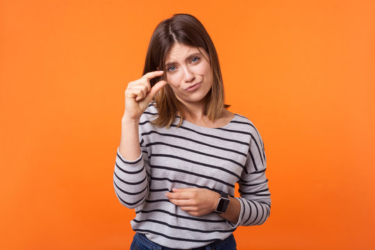 Small amount. Portrait of adorable beautiful woman with brown hair in long sleeve striped shirt showing little bit gesture and looking pleadingly. indoor studio shot isolated on orange background