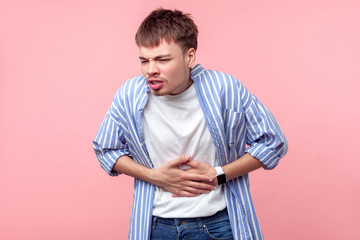 Stomach ache. Portrait of sick brown-haired man with small beard and mustache in casual shirt touching belly suffering abdominal pain, gastritis or constipation. indoor, isolated on pink background