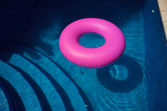 Bright pink inflatable ring in sunny blue swimming pool