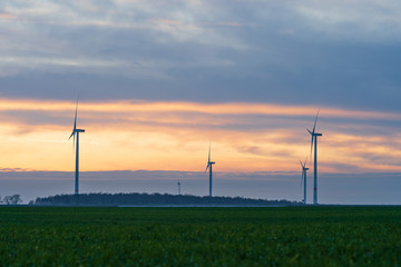 Fototapeta na wymiar germany: wind turbines, windmills in the sunset, green grassland yellow orange sky with clouds 
