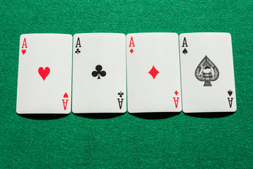 Top view of poker deck aces, lined up, on green playing mat, horizontal