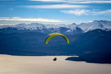 Paragliding over Nahuel Huapi lake and mountains of Bariloche in Argentina, with snowed peaks in the background. Concept of freedom, adventure, flying