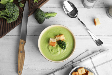 Delicious broccoli cream soup with croutons served on white wooden table, flat lay