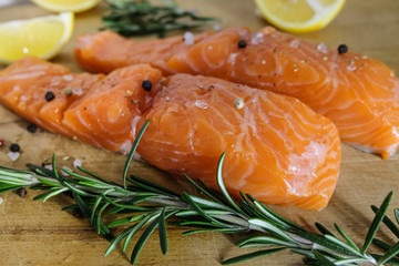 Two salmon or trout steaks on a wooden cutting board with fresh rosemary, chopped lemon, peppercorns and sea salt crystals. horisontal orientation.