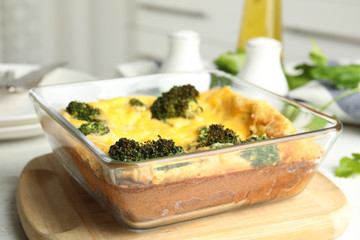 Tasty broccoli casserole in baking dish on wooden board, closeup