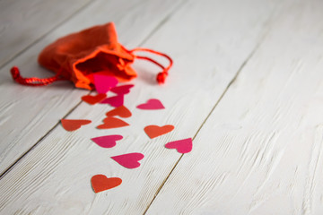 A red bag with spilled hearts on a white wooden surface