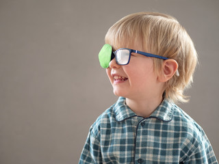 Portrait of funny child in new glasses with green spot to correct strabismus.Orthopedic Boys Eye...