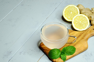 ginger tea in a glass beside mint and lemon on wooden background