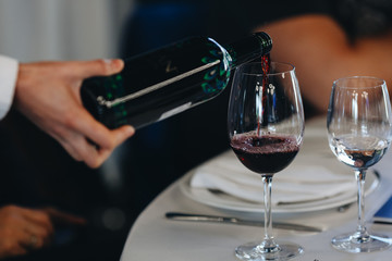 waiter's hand pours red wine into a glass