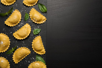 Fototapeta na wymiar Raw ravioli with basil on black table, flat lay and space for text. Italian pasta