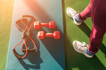 Woman feet near mat with expander and dumbbells