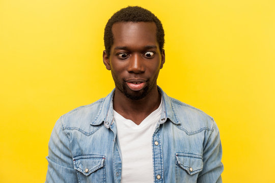 Portrait of silly funny positive man in denim casual shirt crossing eyes looking at his nose, fooling around and having fun, easy optimistic lifestyle. indoor studio shot isolated on yellow background