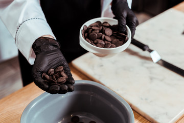 cropped view of chocolatier holing dark chocolate chips in hand
