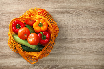 Net bag with vegetables on wooden table, top view. Space for text