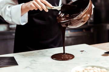 cropped view of chocolatier pouring melted chocolate on marble surface - obrazy, fototapety, plakaty