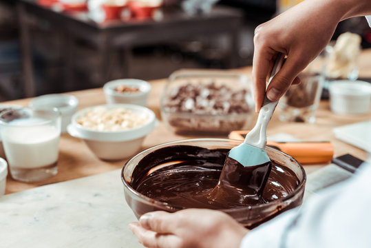 cropped view of chocolatier holding silicone spatula while mixing chocolate in bowl