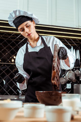 selective focus of chocolatier in apron holding ice tray with melted chocolate near bowl
