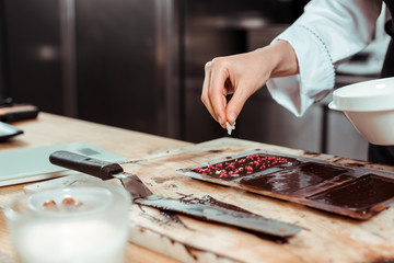 Fototapeta na wymiar cropped view of chocolatier adding coconut flakes on dark chocolate bar