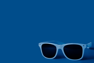 Sunglasses on a blue background, tinted in the trendy classic blue color of 2020. Copy space