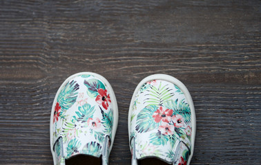 colored kids shoes with tropical floral print on wooden background. Top view