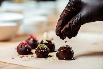 cropped view of chocolatier in black latex glove adding chocolate shavings on fresh made candies