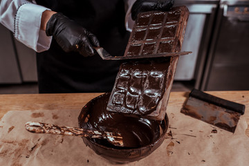 cropped view of chocolatier holding cake scraper near chocolate molds and bowl with melted dark chocolate