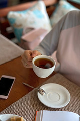 Close up. The girl holds a Cup of tea, a notebook and a phone nearby.