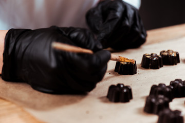 cropped view of chocolatier holding brush near prepared chocolate candies