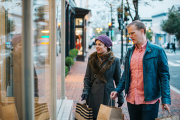 Caucasian couple wearing warm clothing window shopping from outdoors in the winter time. 