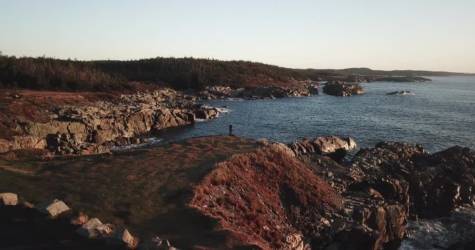 Cinematic Aerial of Man Standing Alone on Hill Over Rocky Coast of Ocean