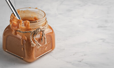 Homemade caramel sauce in a glass jar on a light table. Close-up, copy space. Sweet dessert.