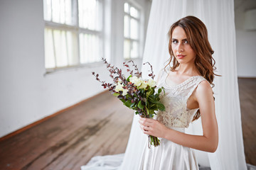 Beautiful bride in a wedding dress in a bright stylish Studio. Wedding in European style. Decor and bouquet in hand.