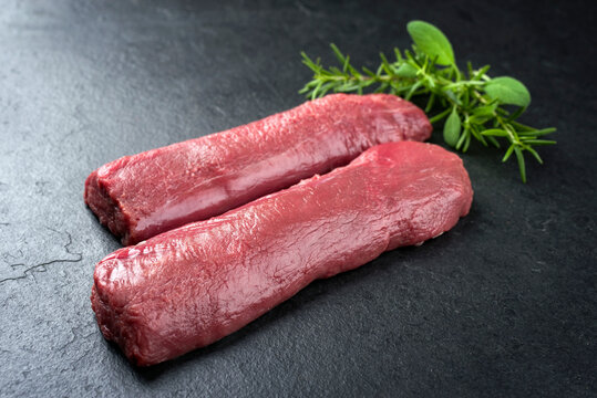 Rohes dry aged Hirsch Filet Steak mit Kr&auml;uter angeboten als closeup auf einem Modern Design Board