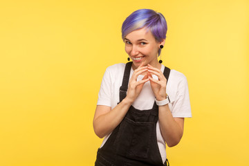 Portrait of sly hipster woman with violet short hair in denim overalls smirking and looking at...