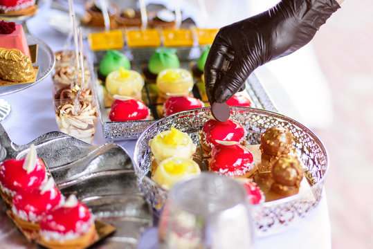 Hands in black gloves serves sweets. Catering