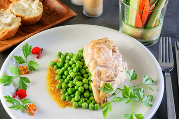 Fried chicken breast with green broiled peas on the white festive dish on the dark background. Healthy food, diet concept.