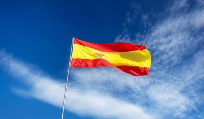 Spanish flag on a pole, undulating in the wind on blue sky with soft white clouds