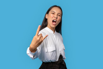 Freestyle. Young woman wearing shirt and skirt standing isolated on blue showing rock gesture...