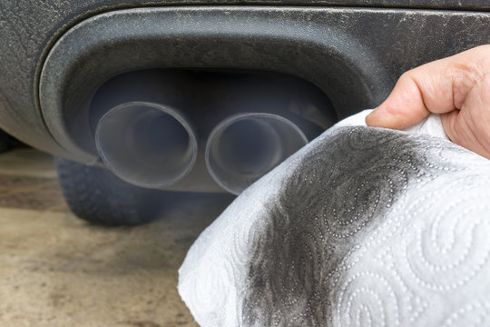 Hand holding a dirty white cloth in front of the smoking exhaust of a car with diesel engine.