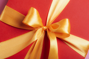 red gift box tied with a golden ribbon. Ribbon tied with a bow on a box. gift concept