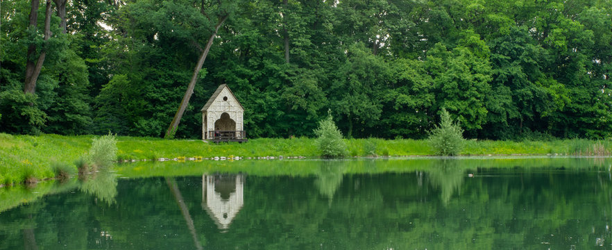 Panorama of a beautiful green scenery in Maksimir park with a small wooden house during summer in Zagreb. Green tree reflections in the water