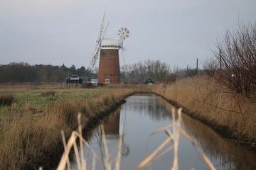 Beautiful rural landscape windmill brick building old brick vintage building Horsey Pump with wooden white sails on Norfolk Broad water canal flat en land East Anglia England cold pink sky reflected
