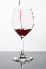 Red wine pouring into clean glass on white background with bubbles. Tasty wine being poured in wine glass. Studio shot
