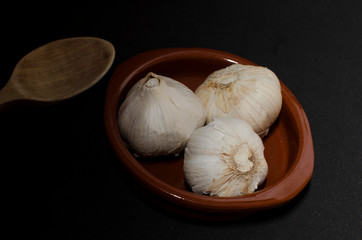 three garlic in clay pot with wooden spoon