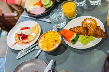 Hotel breakfast with fruits, cereal, juice, bread and pancakes.