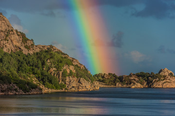 Intense rainbow rising above cliffs.