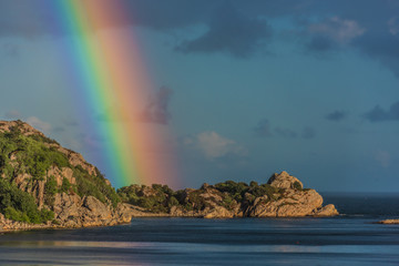Intense rainbow rising above cliffs.