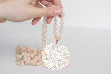 Woman is holding light pink beaded necklace in delicate hands